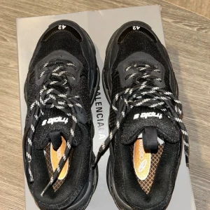 Balenciaga Triple S svarta sneakers - Äkta Balenciaga Triple S sneakers i svart med chunky plattformssula och brokiga snören. Ovandel i mesh och skinn, detaljerad med 'triple s' på tungan och storleken på tån. Snygg och modern siluett som sticker ut, perfekt för dig som gillar statement-skor. Pris kan diskuteras!