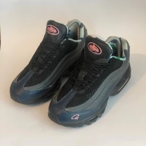 Nike airmax 95s  - Unika Nike Air Max sneakers i svart och mörkblått med coola camo-mönstrade innersulor i grönt, blått och vitt. Skorna har rosa detaljer och synlig Air Max-dämpning i sulan. Ovandelen är i mesh och syntet med snörning för perfekt passform.