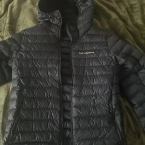 Blå dunjacka Peak Performance S - Säljer en blå dunjacka från Peak Performance i storlek S. Jackan har huva, dragkedja och är quiltad med horisontella sömmar. Perfekt för kalla dagar och har en clean, sportig look. Klassisk logga på bröstet och två sidofickor med dragkedja.