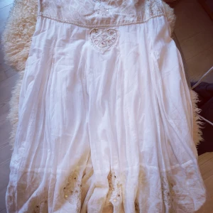 Vit långklänning från Culture [S]  - Säljer en vit långklänning från Culture med broderade detaljer, paljetter och hjärtformade inslag. Nyskick. Klänningen har en romantisk känsla med volangliknande fall och är tillverkad i ett lätt bomullstyg. Perfekt för sommarens alla tillfällen!