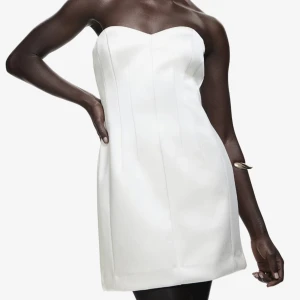 Vit axelbandslös kortklänning H&M NY!  - Snygg vit axelbandslös kortklänning från H&M i stilren design. Klänningen har en figurnära passform och är tillverkad i ett mjukt bomullsmaterial. Perfekt för dig som gillar minimalistisk stil och vill ha en enkel men chic look. Väldigt liten i storleken. Skulle mera uppskatta den som en M