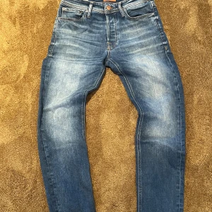 Blå jeans från Jack & Jones - Snygga blå jeans från Jack & Jones med klassisk femficksdesign och ljusa slitningar framtill och baktill. Jeansen har normal passform och raka ben, tillverkade i mjukt denimtyg. Perfekta för dig som gillar en tidlös och avslappnad stil.