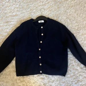 Mörkblå kofta från Gina Tricot - Mysig mörkblå kofta från Gina Tricot i ullblandning. Klassisk rak modell med rund halsringning och snygga kontrasterande knappar framtill. Perfekt att slänga över en t-shirt eller linne för extra värme under kyliga dagar.