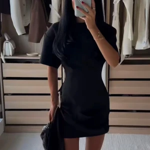 Svart kort klänning med metallspänne Lioness - Stilren svart kort klänning med markerad midja och coolt metallspänne på sidan. Klänningen har korta ärmar och en tight passform som framhäver siluetten. Perfekt för dig som gillar minimalistisk och trendig stil.💓