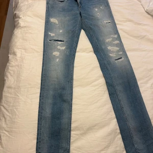 Replay Broken Edge ljusblå jeans 27/32 - Snygga ljusblå jeans från Replay, modell Broken Edge Luz. Jeansen har slitna detaljer och hål framtill för en cool, avslappnad look. Klassisk femficksmodell med dragkedja och knapp. Tillverkade i bomull med en rak passform.