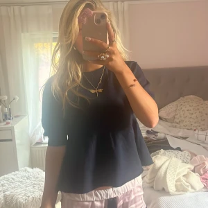 Mörkblå blus med kort ärm - Säljer en mörkblå blus med rund halsringning och korta ärmar. Modellen är lätt utsvängd nedtill och har en enkel, stilren design utan synliga detaljer. Perfekt för dig som gillar en klassisk och avslappnad look.