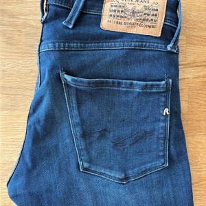 Replay Anbass jeans mörkblå W28 L32 - Snygga Replay Anbass jeans i mörkblå tvätt med klassiska femficksdetaljer och diskret logga på bakfickan. Modellen har smal passform och raka ben, tillverkade i mjukt jeanstyg som sitter skönt hela dagen.