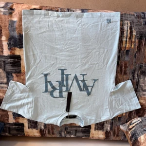 Ljusblå t-shirt från AMIRI - Snygg ljusblå t-shirt från AMIRI med stor tryckt logga framtill i blått och liten logga uppe vid axeln. Klassisk passform och rund halsringning. Tillverkad i mjuk bomull som känns skön mot huden. Perfekt för dig som gillar stilrena och trendiga plagg.