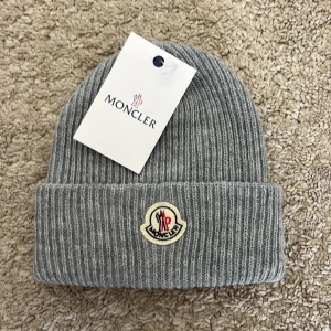 Mössa - Snygg grå ribbstickad mössa med klassisk uppvikt kant och broderad logotyp framtill. Tillverkad i mjuk ull som håller dig varm under kalla dagar. Perfekt accessoar för en clean och stilren look.