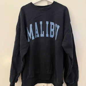 Tröja  - Säljer en mörkblå sweatshirt från Brandy Melville med  ljusblått 'Malibu'-tryck på framsidan i storlek onesize. Använd ett fåtal gånger men bra skick!! 🙌🏽