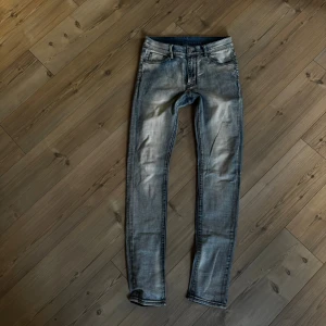 Slim fit jeans från mnml, gråblå - Slimmade jeans från mnml i en snygg gråblå tvätt med slitningar och klassiska fem fickor. Byxorna har låg midja och raka ben, med läderpatch bak i midjan. Perfekt för dig som gillar streetwear och vill ha en cool look.