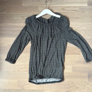 Svart offshoulder blus från KappAhl - Säljer en svart offshoulder blus från KappAhl med vitt geometriskt mönster. Blusen har långa ärmar med resår vid ärmslut och en bred resår upptill som ger en snygg offshoulder-look. Materialet är mjukt och stretchigt, perfekt för dig som gillar bekväma och coola plagg.