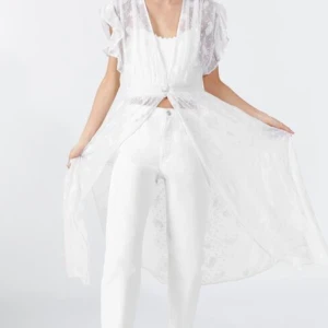 Vit kimono / klänning spets Zara strl S - Drömmig vit långklänning/kimono från Zara med transparent spets och broderade detaljer. Klänningen har v-ringad front, volangärmar och en knapp i midjan. Perfekt för dig som gillar romantisk och bohemisk stil. Lätt och luftig. Storlek S. Längd ca 127cm