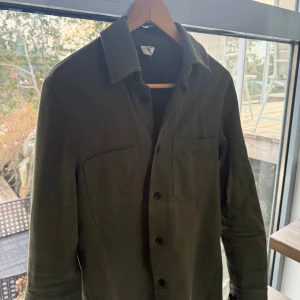 Olivgrön overshirt från arket  - Olivgrön overshirt från arket. Den är använd sparsamt under ett kortare tag. Säljer då den blivit för liten för mig. Finns en lite defekt som är en typ av missfärgning men det syns inte så länge man inte tänker på det. 