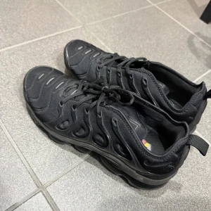 Nike Air max Plus svarta sneakers - Nike Air max Plus i helsvart färg med snyggt vågigt mönster på ovansidan och platt sula med synliga luftkuddar. Skorna har snörning och är tillverkade i syntetmaterial med textilinslag. Perfekt för dig som gillar sportig och modern stil. köpt för 2200, pris går att diskutera, som nya