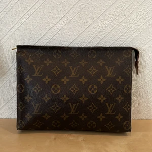 Louis Vuitton monogram kuvertväska - Snygg kuvertväska från Louis Vuitton i klassiskt brunt monogrammönster. Väskan har rektangulär form, dragkedja upptill och är tillverkad i skinn med detaljer i läder. Perfekt för att bära det viktigaste med stil.