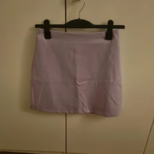 Ljuslila kortkjol från Monki - Säljer en stilren ljuslila kortkjol från Monki i storlek 36. Kjolen har en enkel och rak passform, perfekt att matcha med en crop top eller oversized hoodie. Materialet känns mjukt och lätt, vilket gör den skön att bära under varmare dagar.