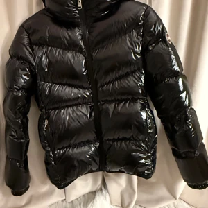 Svart dunjacka från Colmar - Säljer en svart, glansig dunjacka från Colmar. Jackan har två fickor med dragkedja och en tydlig Colmar-logga på ärmen. Perfekt för kalla dagar.
