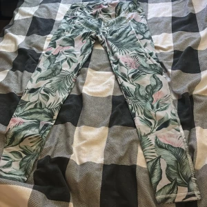 Mönstrade leggings med tropiska blad - Snygga leggings från Cubus i storlek M med tropiskt bladmönster i grönt och rosa på ljus botten. Hög midja och tight passform, perfekta för träning eller chill. Materialet är mjukt och stretchigt syntet som sitter skönt mot kroppen.