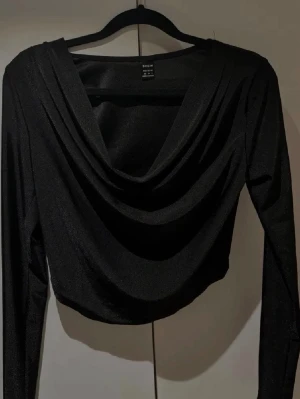 Svart croppad topp från SHEIN - Säljer en svart croppad topp från SHEIN med draperad front och lång ärm. 