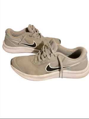 Nike Star Runner grå sneakers - Nike Star Runner sneakers i ljusgrå färg med svart och vit swoosh på sidan. Perfekta för träning eller chill vardagsstil. Snygg och enkel design.