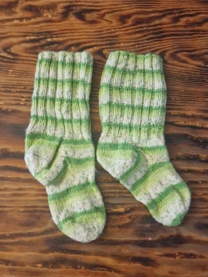 Grönrandiga stickade sockor - Stickade sockor i grönt och vitt med randigt mönster. Mjuka och sköna, perfekta för kalla dagar. Ribbstickad skaft och klassisk form. Saknar storleksmärkning men om man mäter från tå till häl så är de ca 16-16.5 cm vilket motsvarar ungefär stl 26 - 27.