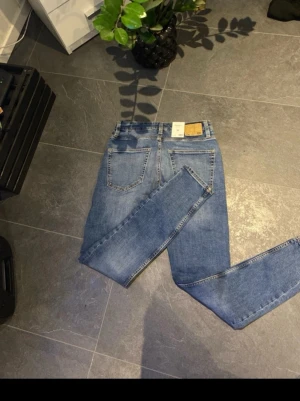 Blå jeansbyxor från C, storlek 30/32 - Säljer ett par klassiska blå jeansbyxor från C i storlek 30/32. De har fem fickor, gul kontrastsöm och stängs med dragkedja och knapp. Jeansen har en rak passform och är tillverkade i slitstarkt denimtyg. Perfekt för dig som gillar enkel och tidlös stil.