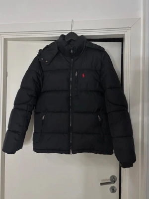 Svart pufferjacka från Polo Ralph Lauren - Svart pufferjacka från Polo Ralph Lauren med röd logga på bröstet. Köpt ifrån Zalando för 3597 kr säljs då jag redan har börjat använda en annan jacka. Pris går att diskutera!
