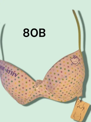 Hello Kitty prickig bh 80B - Söt bh från Hello Kitty i storlek 80B med pastellfärgade prickar på vit botten. Axelbanden är ljusgröna och det finns en liten rosett framtill. Bh:n har tryckt Hello Kitty-logga och motiv på kupan. Perfekt för dig som gillar gulliga detaljer. Varan är oanvänd och kommer från ett konkurslager från 2000-talet. I många fall är prislappen kvar (se bild). Har fler annonser och bra bundlerabatt vid köp av flera.