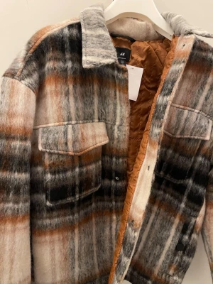 Rutig overshirt från H&M i ullmix - Säljer en riktigt snygg rutig overshirt från H&M i mjuk ullmix. Jackan har stora bröstfickor med lock, knappar framtill och en schysst färgkombo i beige, grått, svart och brunt. Perfekt lager på lager och ger en chill vibe till din outfit.