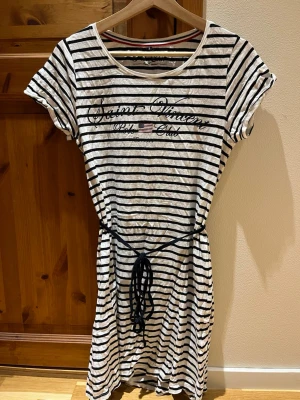 Randig klänning. - Randig klänning i färgerna vitt och mörkblå. Storlek S från Polo Club. Sparsamt och sällan använd. Går ner till ovanför knäna. Text på framsidan där det står ”Saint Vincent, Polo Club, Est 1977. Säljes då den inte används längre. Djur och rökfritt hem.