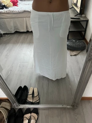 Vit långkjol med snörning  - Säljer en vit långkjol från lager 157 i storlek XS. Kjolen har en rak och enkel design med snörning i midjan och är gjord i mjukt bomullsmaterial. Perfekt för dig som gillar en clean och chill stil. Fråga gärna om fler bilder eller info!