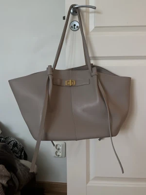 Beige axelväska från Gina Tricot!  - Stilren beige axelväska från Gina Tricot. Väskan har en rymlig insida, långa axelband och snygg guldfärgad vridlåsdetalj framtill. Perfekt för dig som vill ha plats för allt du behöver under din vardag. Dator passar i väskan och innerfickor finns. OBS: Inuti väskan så finns det en fläck på tyget. Väskan tvättas såklart innan den fraktas till försök att få bort fläcken. Banden på väskan har även lite slitage (se bild). Därför säljs väskan lite billigare. Nytt pris: 400kr - Mått 40cm