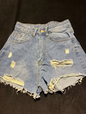 Blå högmidjade jeansshorts från SHEIN - Säljer ett par blå jeansshorts från SHEIN i storlek XS. De är högmidjade med fransiga kanter och slitna detaljer både fram och bak. Klassisk femficksmodell med knapp och dragkedja. Perfekta för en chill sommarlook.