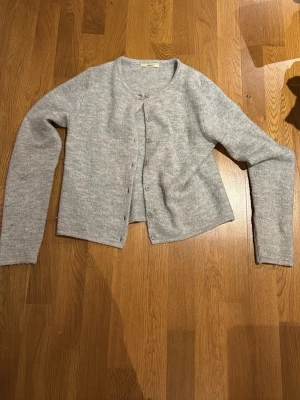 Grå stickad kofta från Gina Tricot - Mysig grå stickad kofta från Gina Tricot i storlek S. Koftan har rund hals, långa ärmar och knappar framtill. Perfekt att slänga på sig när det är lite kyligt. Enkel och stilren design som funkar till många olika outfits.