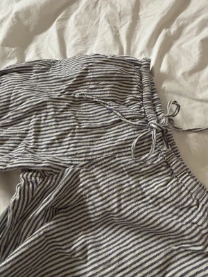 Randiga byxor med snörning - Ett par randiga byxor i vitt och blått. Byxorna har snörning med raka ben i ett linne aktigt material. Perfekta för varma dagar eller softa hemmakvällar. Lätta och luftiga i materialet.