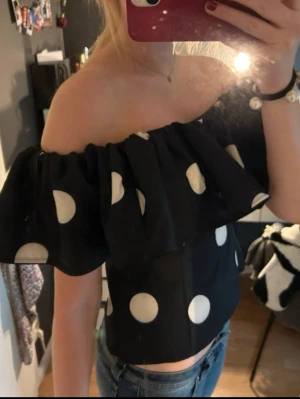 Svart offshoulder topp med vita prickar - Säljer en svart offshoulder topp med stora vita prickar och bred volang runt axlarna. Använd fåtal gånger!!🩵