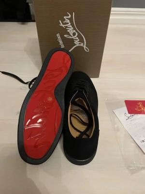 Svarta Christian Louboutin sneakers - Säljer ett par svarta sneakers från Christian Louboutin i mocka med den ikoniska röda sulan. Skorna har snörning och en stilren, rund tå. Kommer med originalkartong och äkthetsbevis. Perfekta för dig som vill ha något exklusivt och tidlöst.
