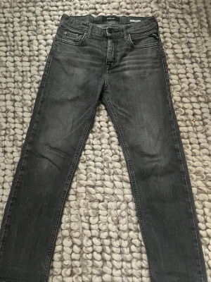 Replay svarta jeans Thad slim fit - Säljer ett par svarta Replay jeans i modellen Thad med slim fit. Jeansen har klassisk femficksdesign, snygga detaljer på bakfickorna och Replay-logga vid myntfickan. Materialet är jeans med en mörk tvätt som ger en cool look, storleken är 142cm