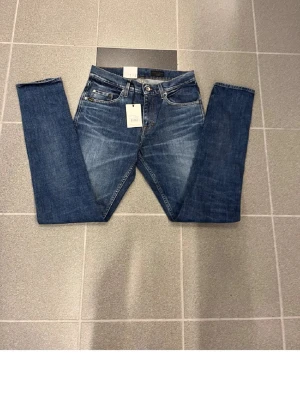 Blå slim jeans från tiger of sweden W29 L34 - Snygga blå jeans från T/J med smal fot. Jeansen har fem fickor, knappgylf och bruna detaljer vid linningen. Perfekt passform för dig som gillar raka ben och tidlös stil. Materialet är slitstarkt jeans och färgen är mörkblå med lätt tvättad look.