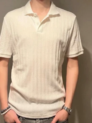 Vit ribbad polotopp från H&M - Säljer en vit ribbad polotopp från H&M i slim fit. Toppen har korta ärmar, klassisk krage och knappar framtill. Materialet är mjukt och lätt, perfekt för en clean och stilren look. Passar dig som gillar minimalistisk stil.