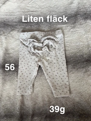 Söta vita leggings med volang - Supersöta vita leggings med små grå blommor och volangdetalj bak. Perfekta för de allra minsta och har en mjuk resår i midjan. Materialet känns mjukt och skönt mot huden, och volangen ger en gullig touch.🌸 Liten fläck. Storlek 56