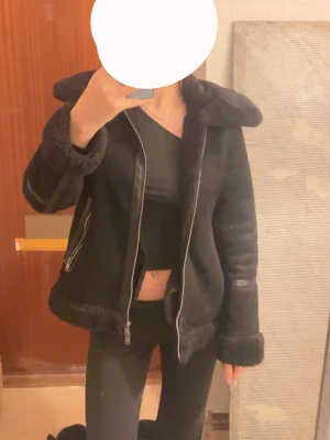 Svart pälsjacka med dragkedja - Säljer en svart pälsjacka med fluffiga detaljer vid krage, ärmslut och nederkant. Jackan har två fickor med dragkedja och en snygg, bred krage. Materialet är pälsimitation och skinn, perfekt för kalla dagar. Stängs med dragkedja framtill.