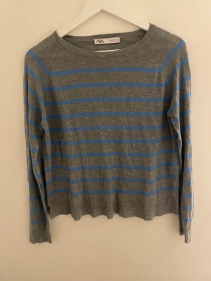 Gråblå randig tröja från Zara - Säljer en tunn, långärmad tröja från Zara i storlek S. Tröjan är grå med blå horisontella ränder och har en rund halsringning. Materialet är mjukt och lätt, perfekt för lager-på-lager under vår och höst. Enkel och stilren design som funkar till jeans eller kjol.
