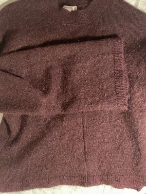 Tröja - Mysig vinröd stickad tröja från Gina Tricot med rund halsringning och långa ärmar. Tröjan har en enkel, rak passform och ribbade muddar vid ärmslut och nederkant. Perfekt för kyliga dagar och enkel att styla till olika outfits.