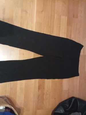 Svarta kostymbyxor med lite lätt utsvängda ben - Snygga svarta kostymbyxor med raka ben och klassisk passform. Byxorna har hög midja och stängs med metallhakar och dragkedja fram. Materialet känns mjukt och har en lätt stretch, perfekt för en clean och stilren look. Det är storlek 34