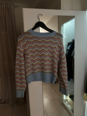 Pastellfärgad stickad tröja från Lindex - Säljer en stickad tröja från Lindex med vågigt mönster i pastellfärger, ljusblå, rosa, beige och vit. Tröjan har ribbade muddar och nederkant samt rund hals. Använd väldigt lite så i väldigt fint skick. Storlek 146/152