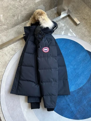 Mörkblå Canada Goose Wyndham - Säljer en mörkblå dunjacka från Canada Goose med ikonisk patch på ärmen och stor huva med fluffig päls. Jackan har långa ärmar, ribbade muddar och praktiska fickor framtill. Perfekt för kalla vinterdagar och riktigt snygg streetstil.