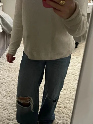 Blåa wide jeans med slitna knän - Säljer ett par blåa högmidjade jeans med breda ben och stora slitningar vid båda knäna. Jeansen har en loose passform och är tillverkade i klassiskt denimtyg. Storlek 32 men stor i storleken💕