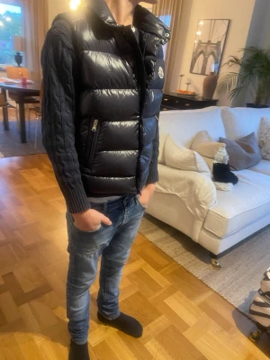 Marinblå dunväst från Moncler, XXS - Säljer en marinblå dunväst från Moncler med stickade ärmar och quiltad framsida. Västen har dragkedja, hög krage och Moncler-logga på bröstet. Perfekt för dig som vill ha en varm look under höst och vinter. Och såklart äkta 